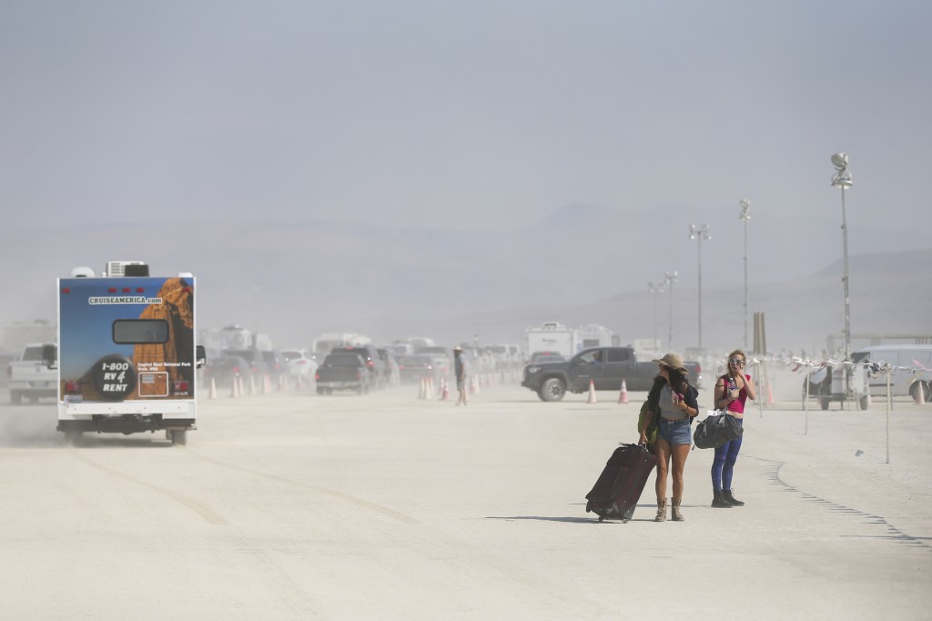 In this Tuesday, Aug. 30, 2016 photo, attendees walk with luggage towards the entrance to Burning Man at the Black Rock Desert near Gerlach, Nev. (Chase Stevens/Las Vegas Review-Journal via AP)